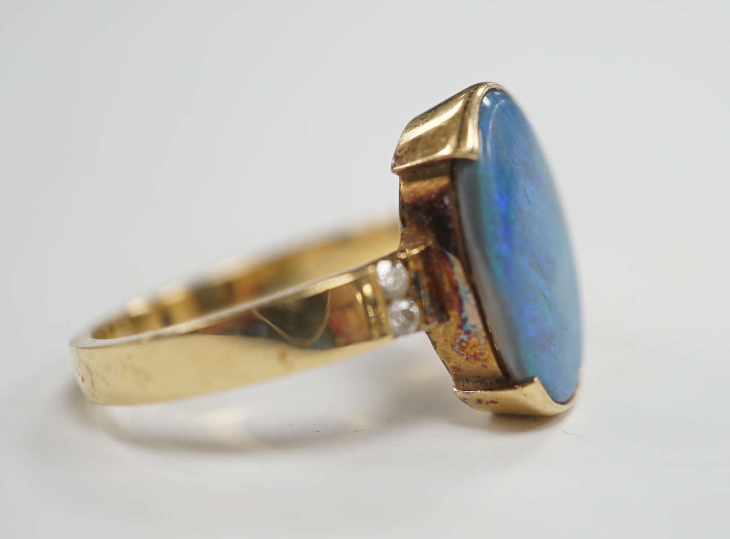 A yellow metal and black opal oval dress ring, with diamond chip shoulders, size P, gross weight 5.7 grams.